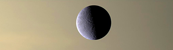 The icy moon Rhea is seen in orbit above the cloud tops of Saturn in this Cassini spacecraft image