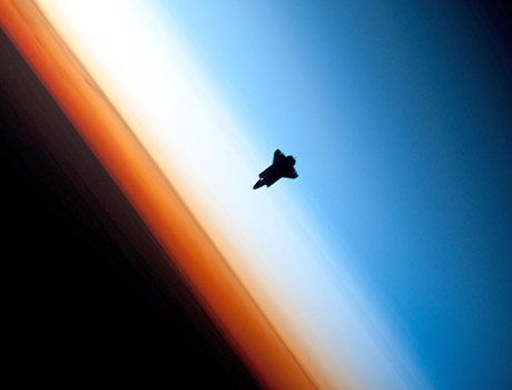 STS-130 image of Space Shuttle Endeavour approaching the ISS as the sun sets in the background