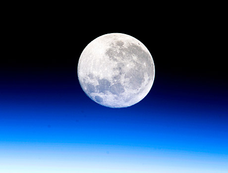 ISS image of a nearly full moon bathed in the blue glow of the Earth's atmosphere
